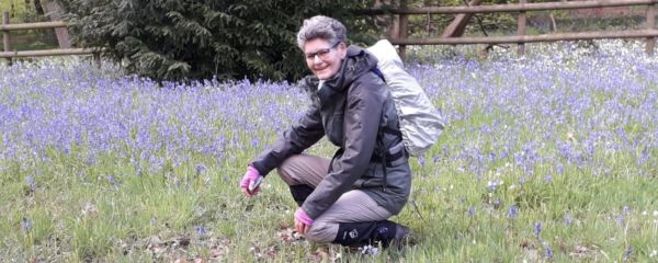 Sue crouching amongst wildflowers whilst on a walk, and smiling to camera